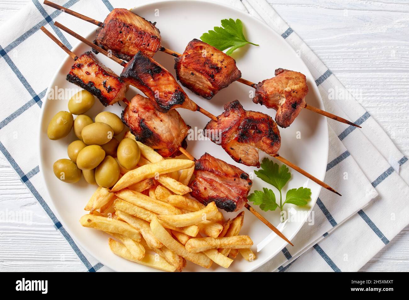 Juicy grilled pork kebabs on a plate with green olives and potato fries, horizontal view from