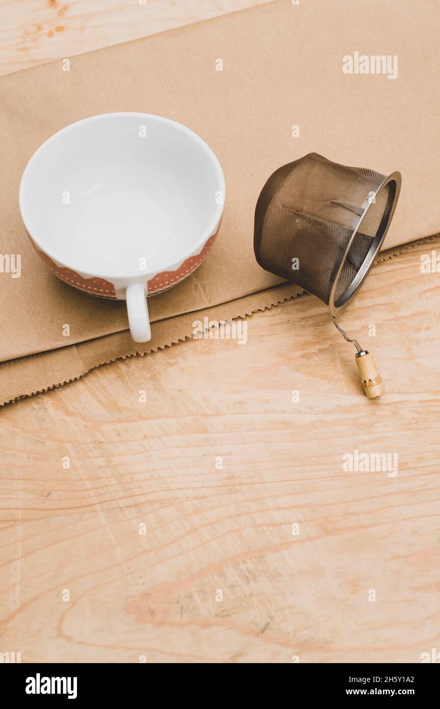 metal tea strainer and tea cup on a brown paper and rustic wooden ...