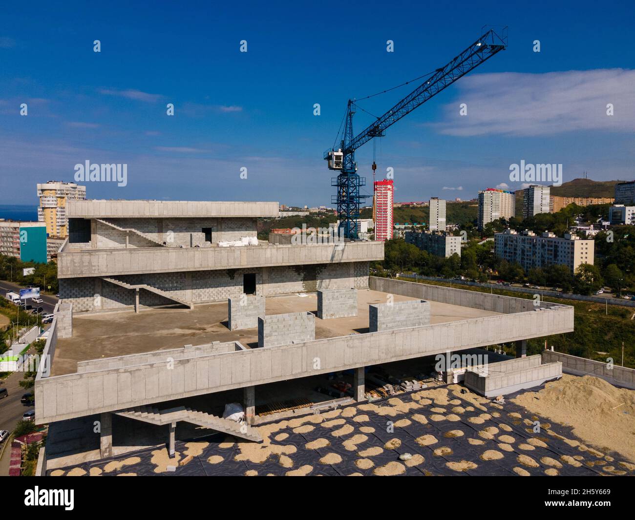 A large gray building under construction in the city. Blue construction crane near the construction site. Stock Photo