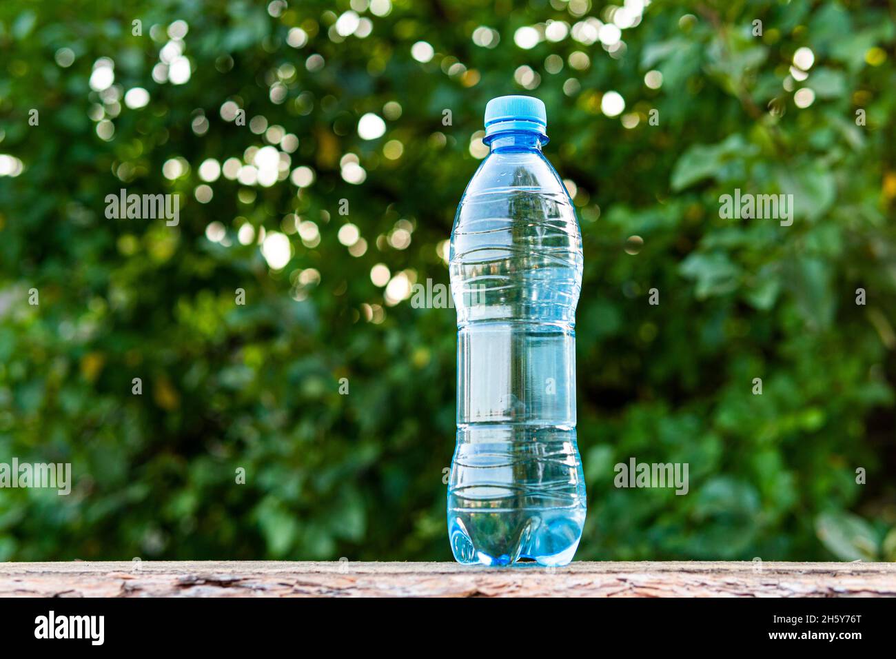 Drinking water pouring from a plastic bottle with blurry green foliage in the backdrop Stock Photo