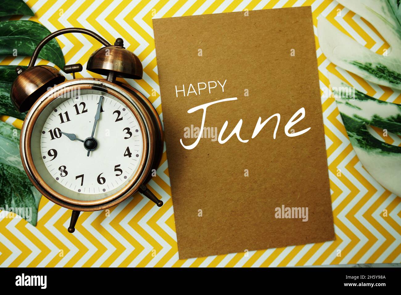 Happy June typography text on paper card with alarm clock and Monstera  leave Stock Photo - Alamy