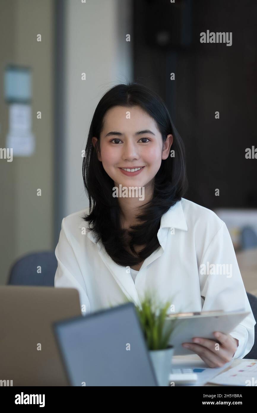 Portrait of young beautiful Asian woman looking at camera in office ...