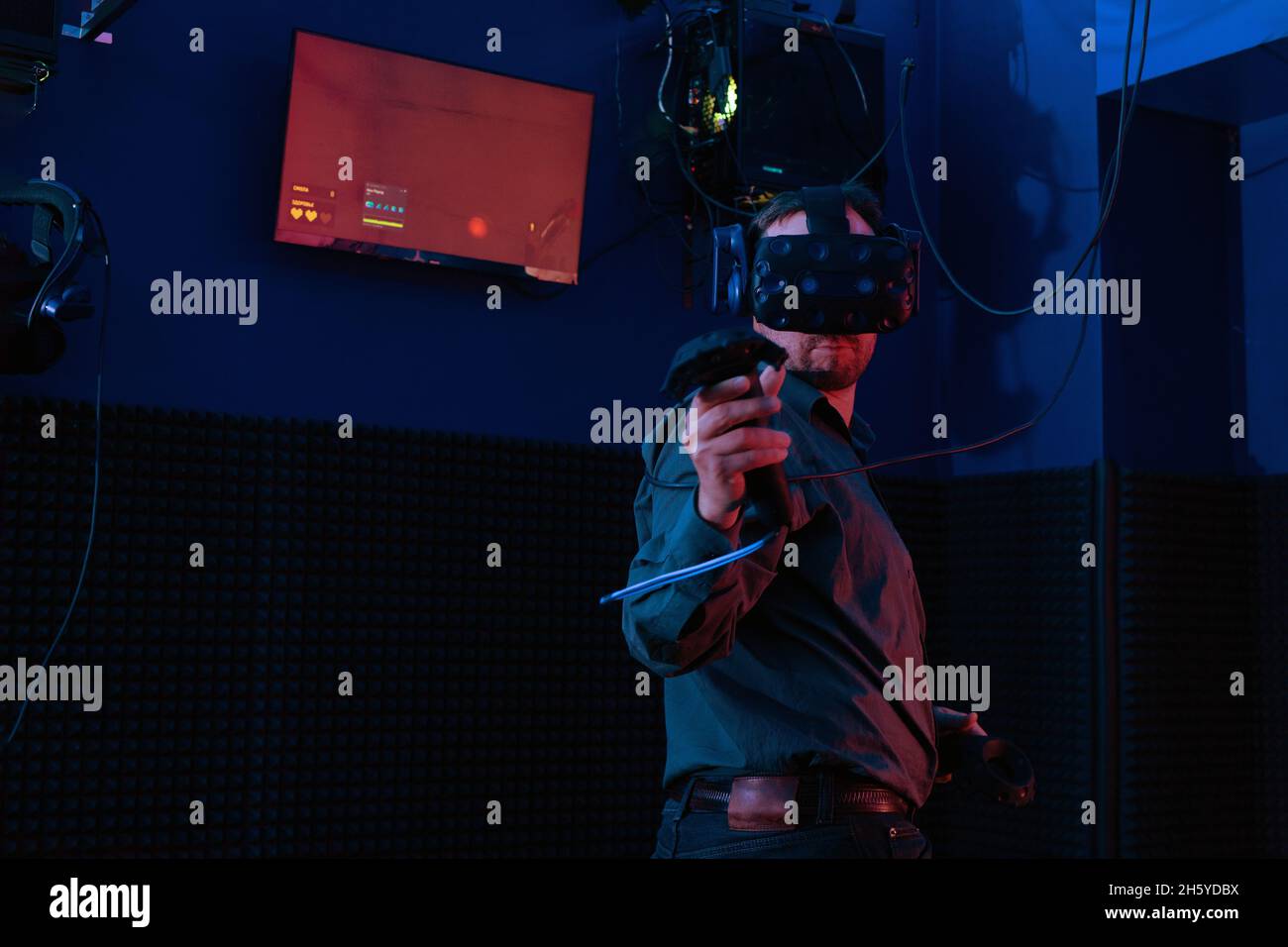Young man in virtual reality helmet using joystick while playing new video game in vr club. Stock Photo
