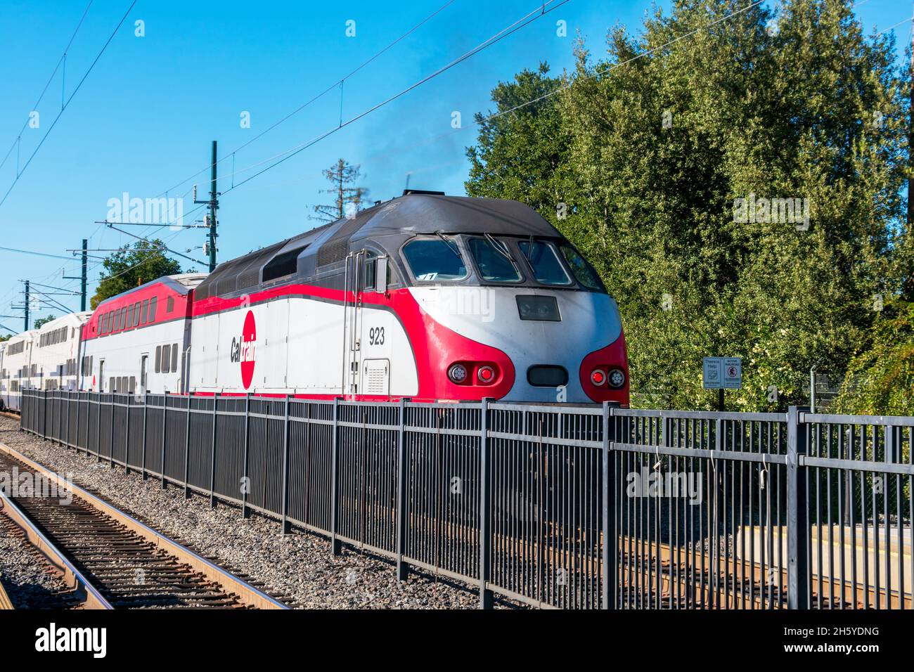 MP36PH-3C diesel locomotive in Caltrain livery, used for Baby Bullet service, belching out black diesel smoke while passing the station behind securit Stock Photo