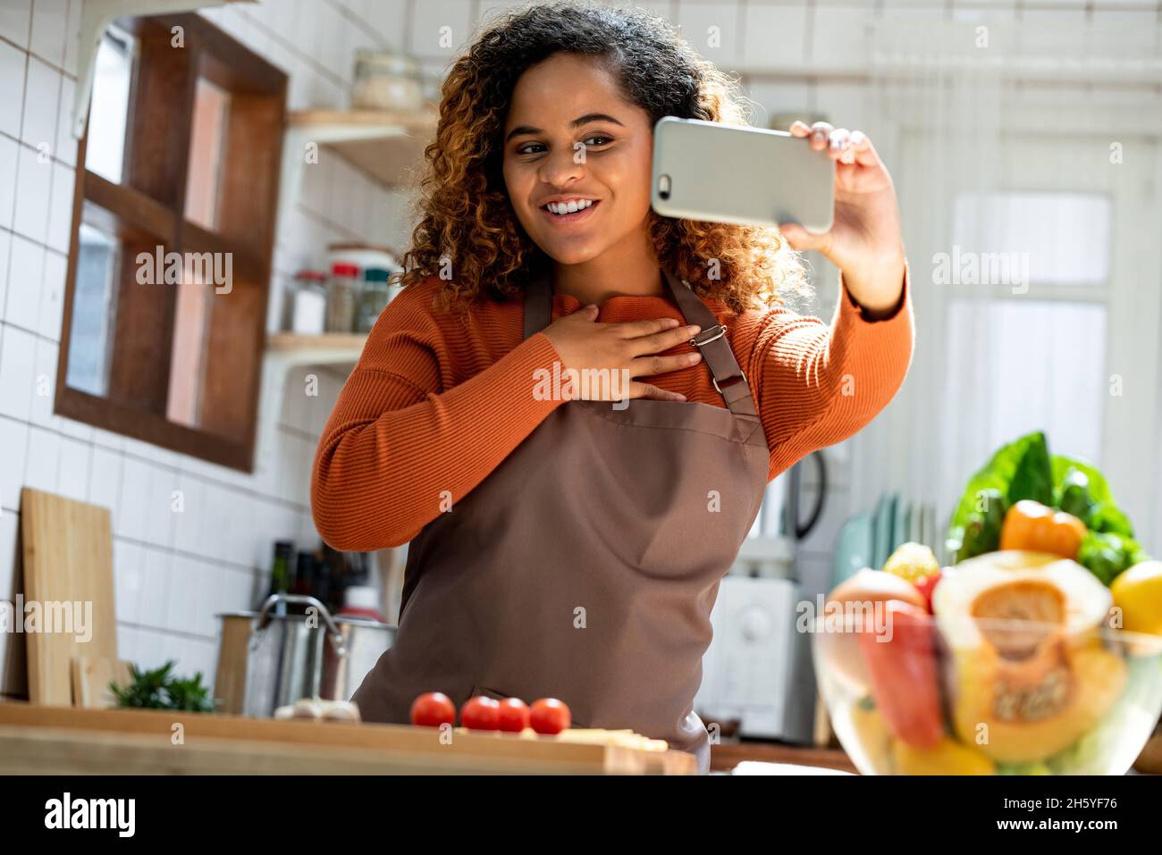 Young African American woman looking at mobile phone making video call while cooking in kitchen at home Stock Photo
