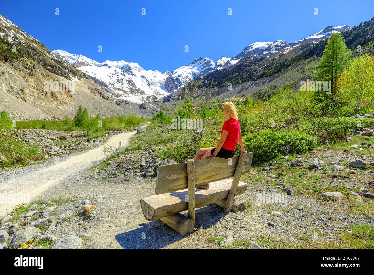 Woman with red t-shirt on the trekking trail to Morteratsch glacier of Switzerland. Biggest glacier in Bernina Range of the Bundner Alps in Grisons Stock Photo