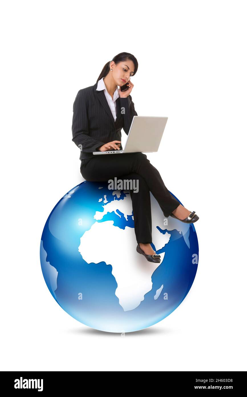 A  female corporate employee working on laptop and talking on phone sittting on graphic earth. Stock Photo