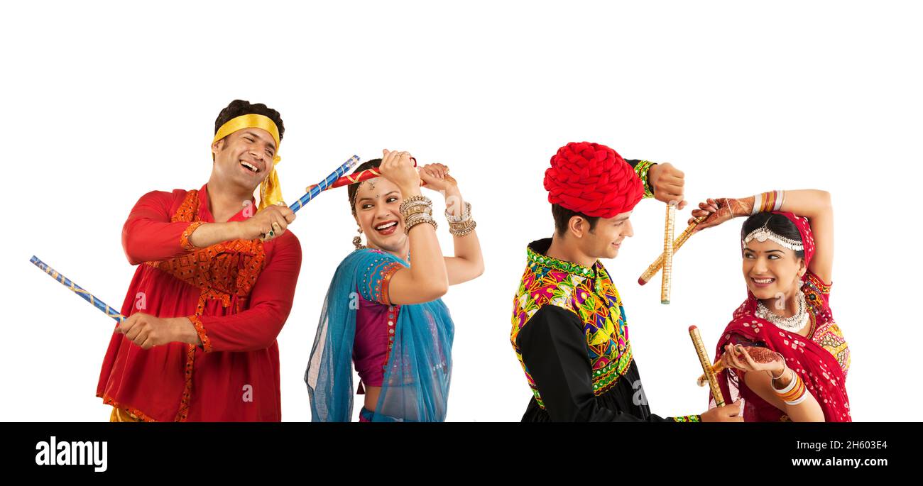 Indian couple dressed in cultural attire doing garba folk dance with dandia sticks. Stock Photo