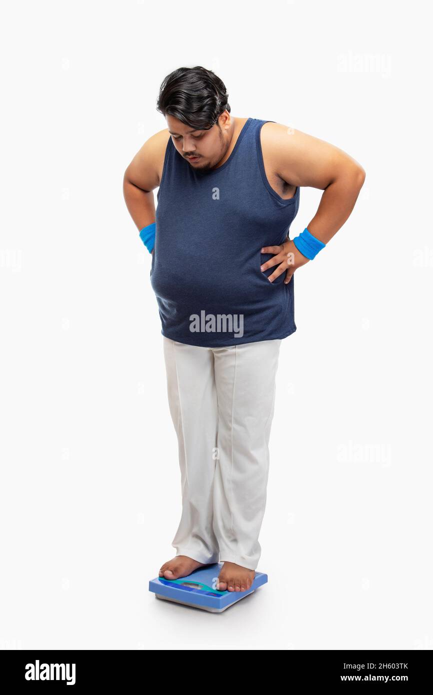 Portrait of a fat man standing on weighing machine and measuring weight. Stock Photo
