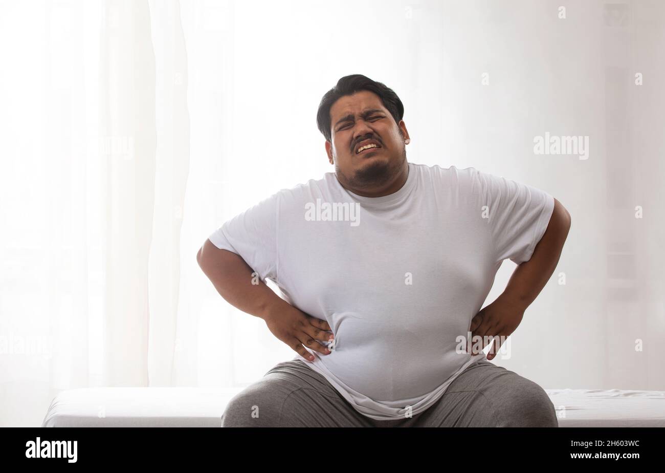 A fat man sitting and holding his belly in pain. Stock Photo