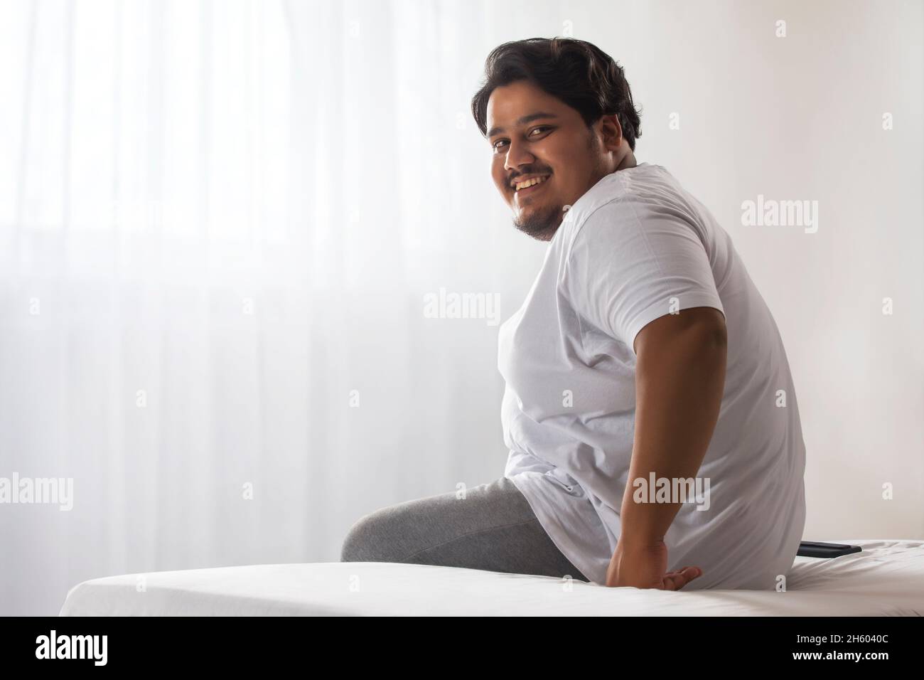 A fat man smiling while sitting in his room. Stock Photo