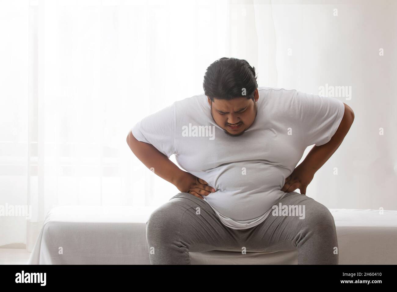 A fat man sitting and holding his belly in pain. Stock Photo