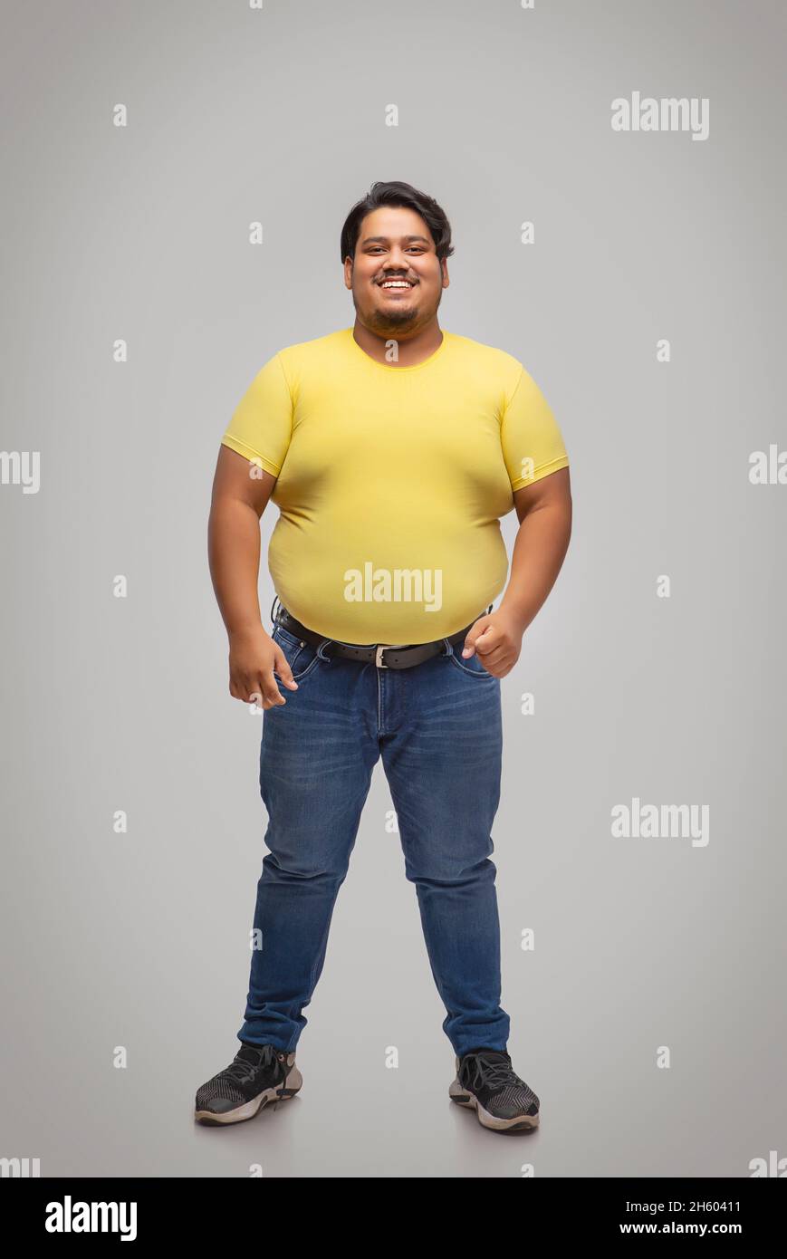 Portrait of a fat man standing and smiling against plain background. Stock Photo