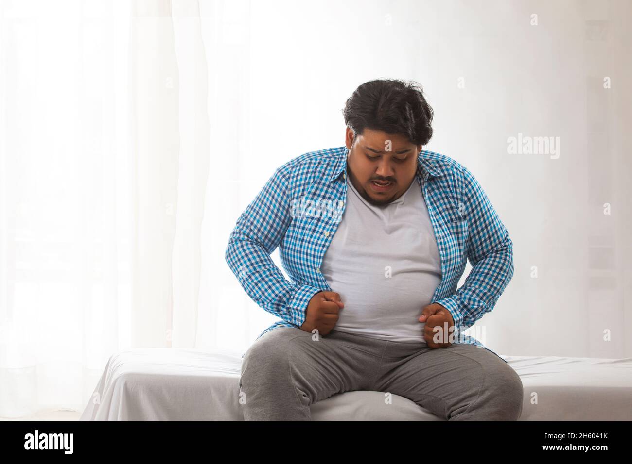 A fat man sitting and trying to wear his shirt. Stock Photo