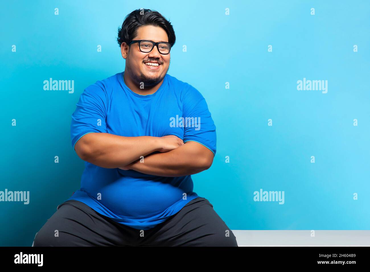 Portrait of a fat man wearing eyeglasses smiling while sitting cross armed. Stock Photo