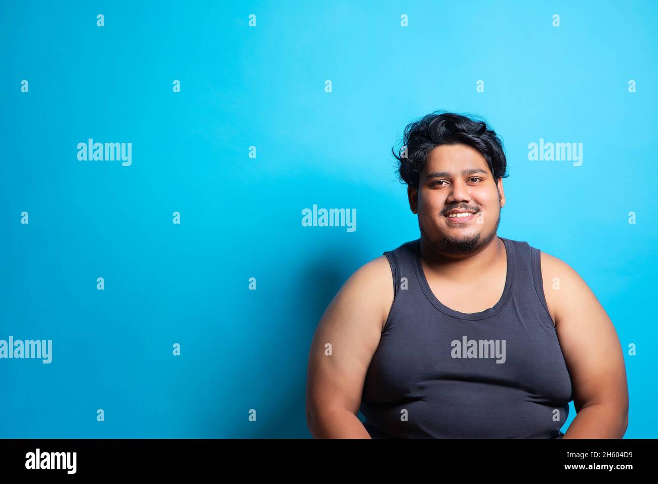Portrait of a fat man sitting and smiling against plain background. Stock Photo