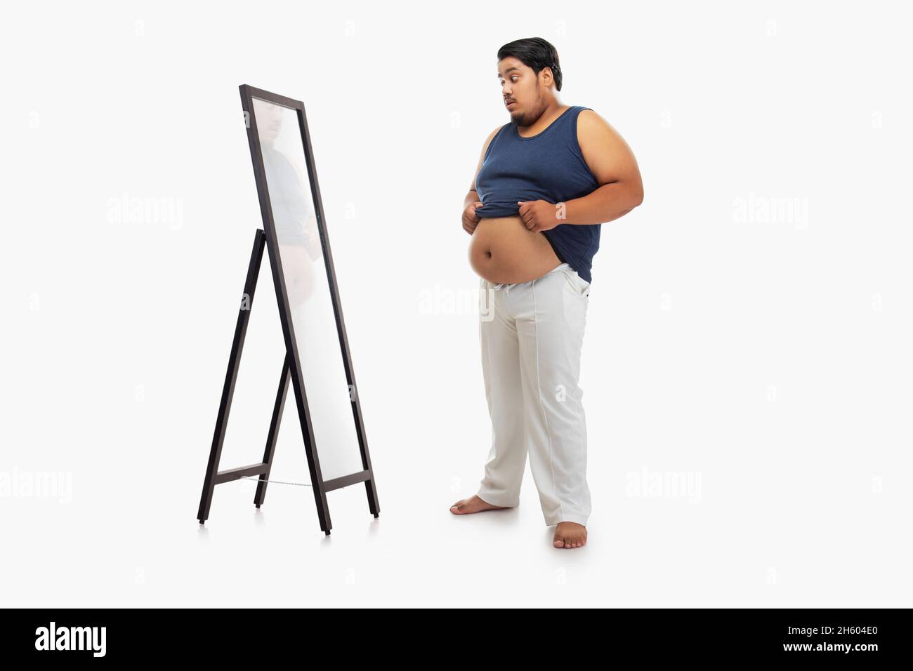 Portrait of a fat man looking at bellyfat in mirror with surprise against plain background. Stock Photo