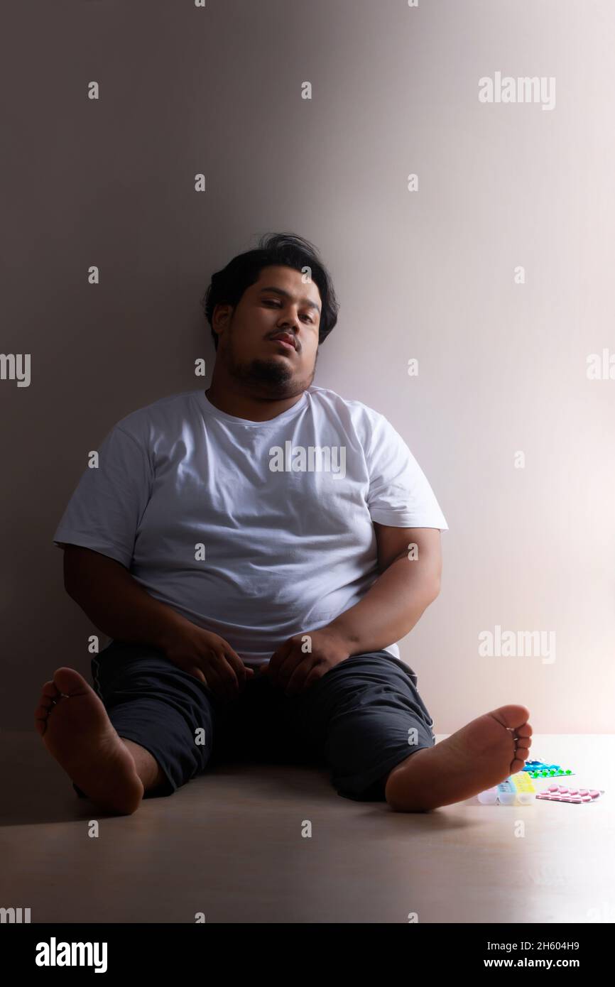 A fat man sitting with pills and medicines kept beside. Stock Photo