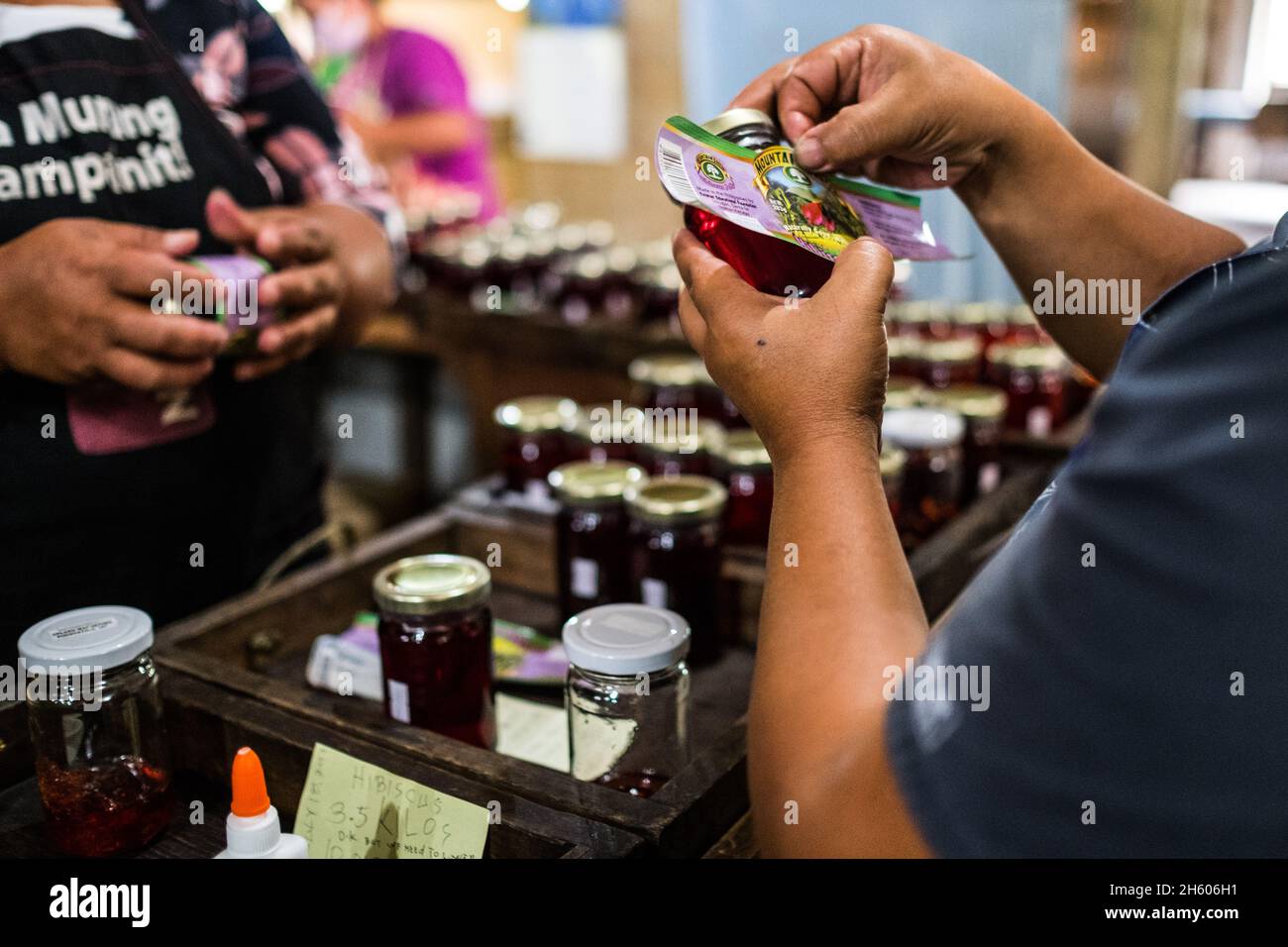 July 2017. Workers applying labels by hand to jars of jelly and other prepared foods are glued and applied by hand. The Kalihan Educational Foundation (KEF) runs a small jam, jelly, and other prepared foods making operation as part of their enterprise development programs. Imugan, Nueva Vizcaya, Philippines. Photograph by Jason Houston for USAID Stock Photo