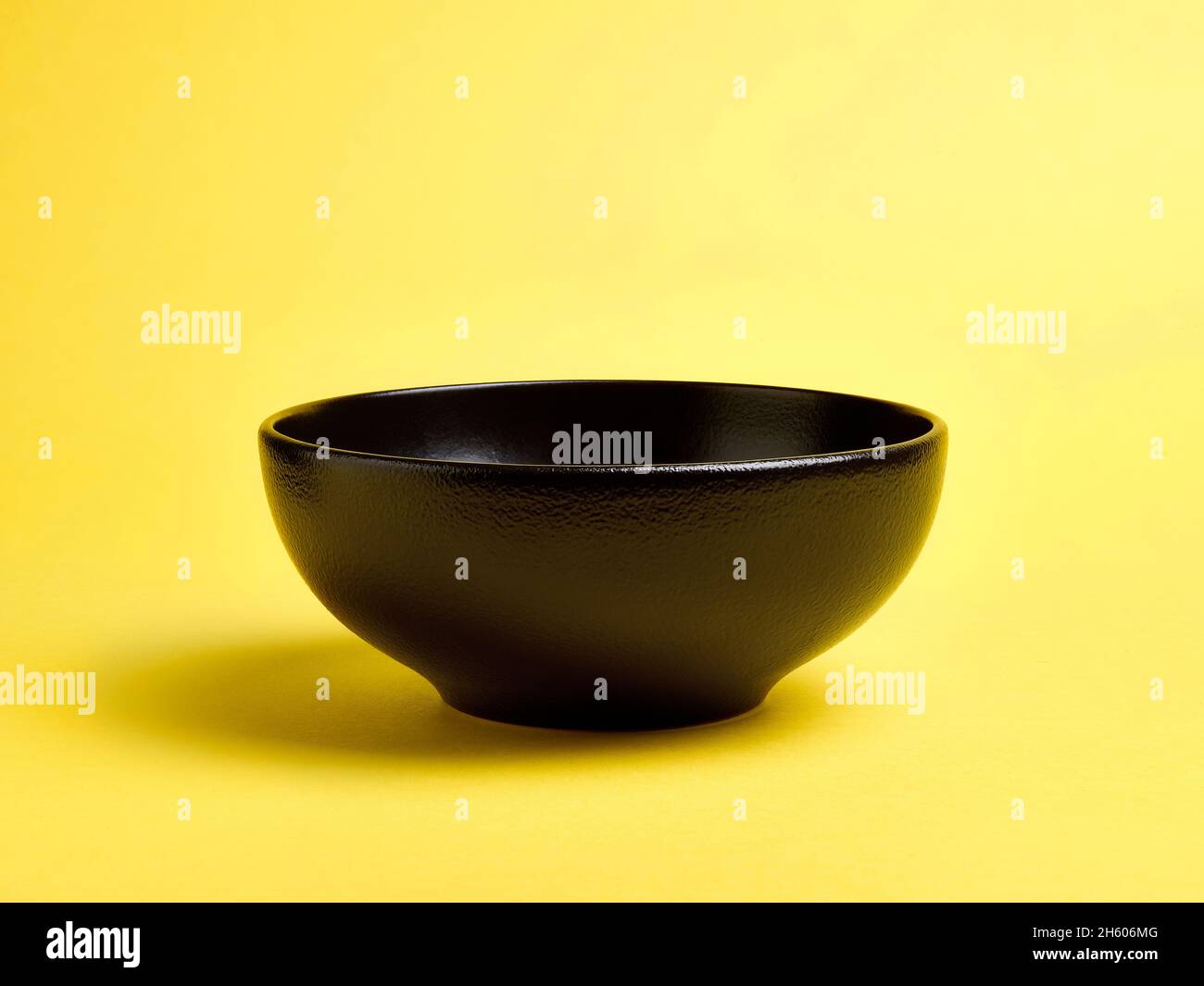 Empty black ceramic bowl on yellow background Stock Photo