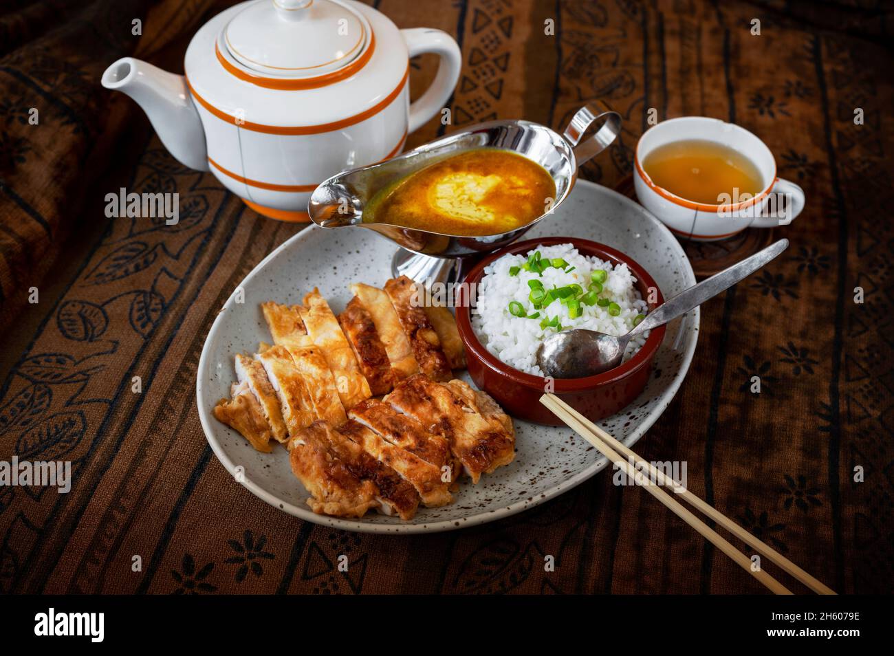 Sliced chicken meat fried in crispy panko bread crumb, stewed rice in bowl, chopstick, spicy  curry sauce in sauce boat, tea in teapot. Asian cuisine. Stock Photo