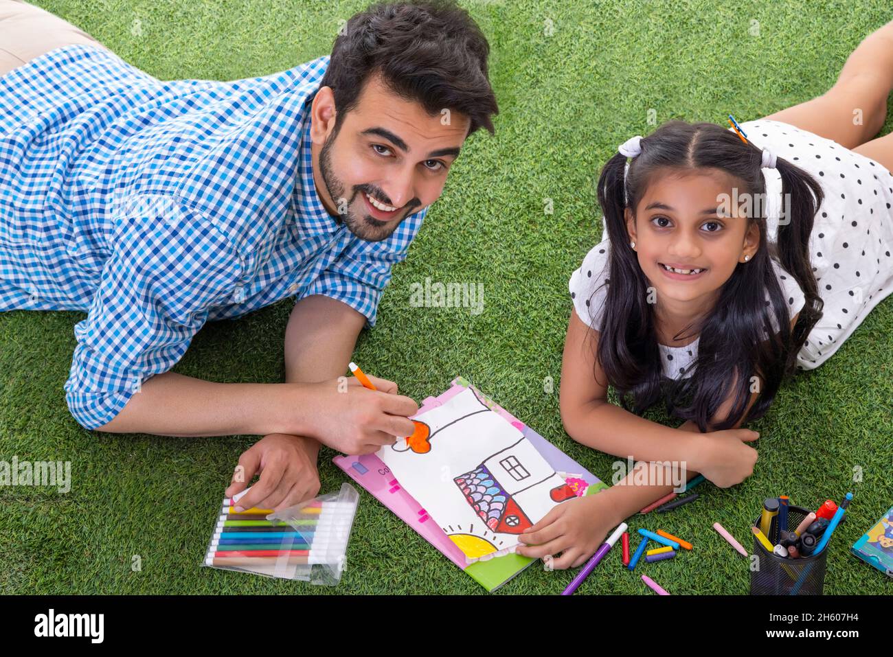 A FATHER AND DAUGHTER LOOKING AT CAMERA WHILE COLOURING TOGETHER Stock Photo