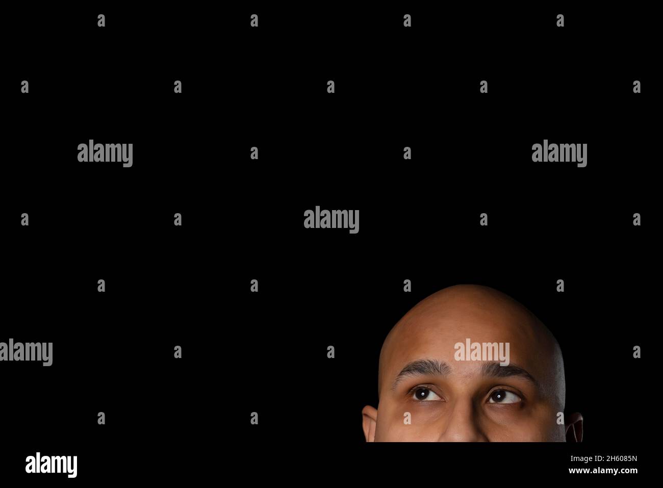 The shaved head and eyes of a bald man looking up against black background. Stock Photo