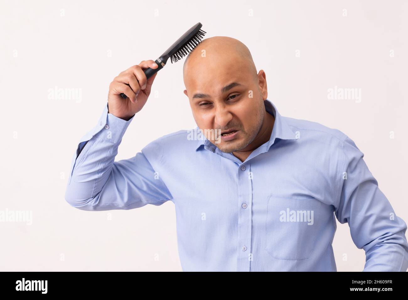 Portrait of a bald man combing his shaved head with frustration against white background. Stock Photo