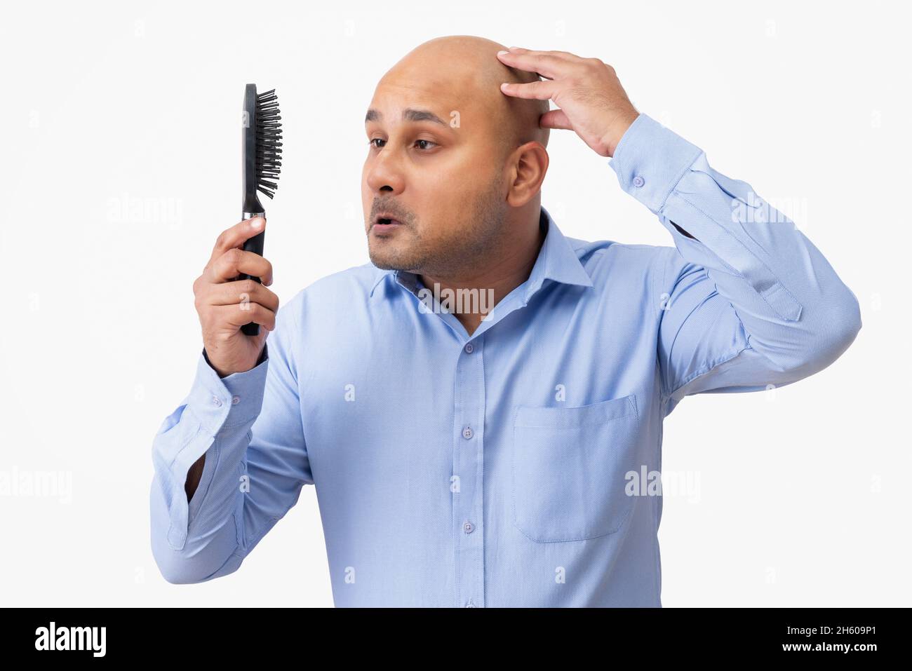 Portrait of a bald man touching his shaved head while looking sadly at comb in his hand. Stock Photo