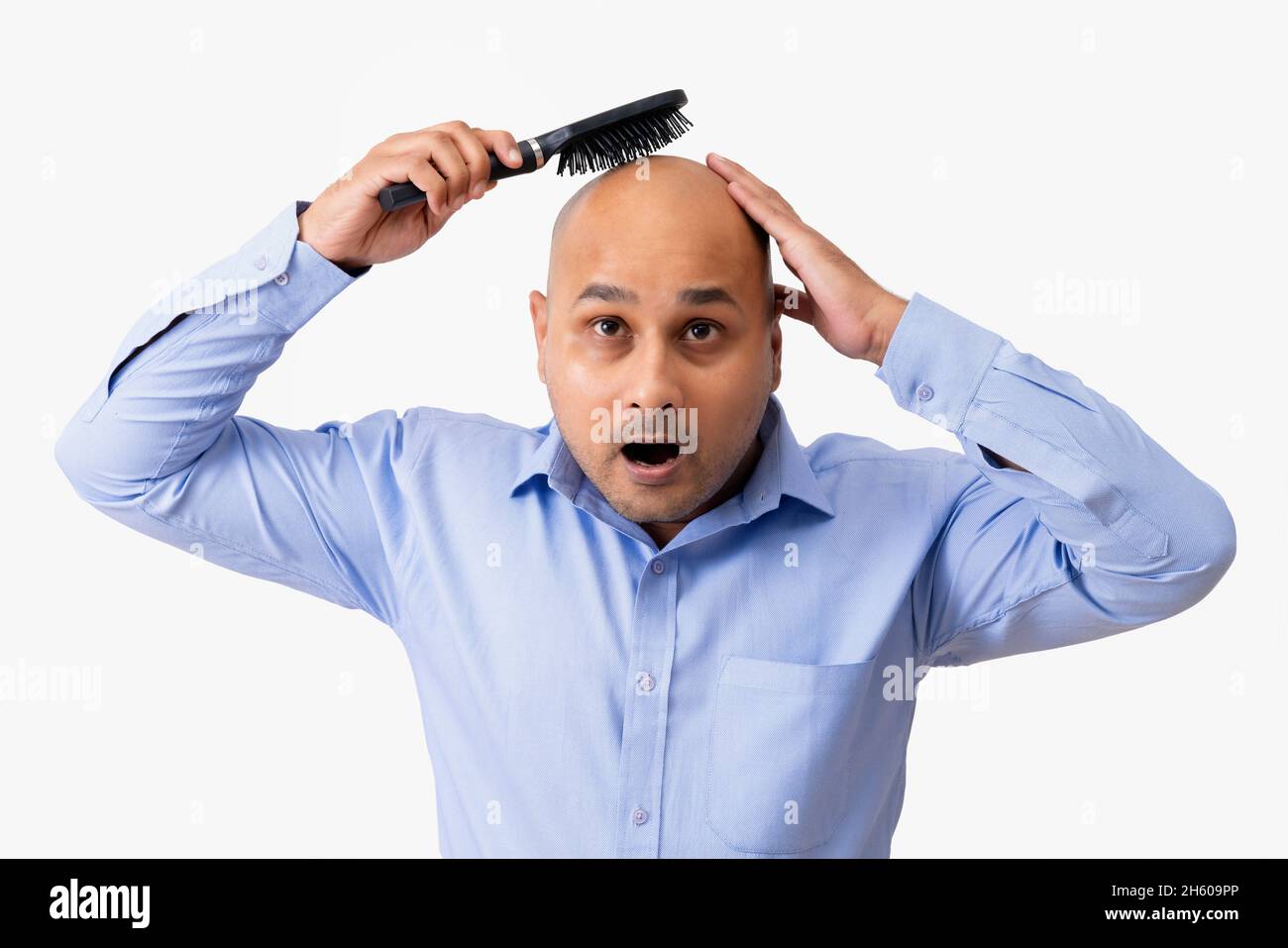 Portrait of a bald man combing his shaved head while gaping against white background. Stock Photo