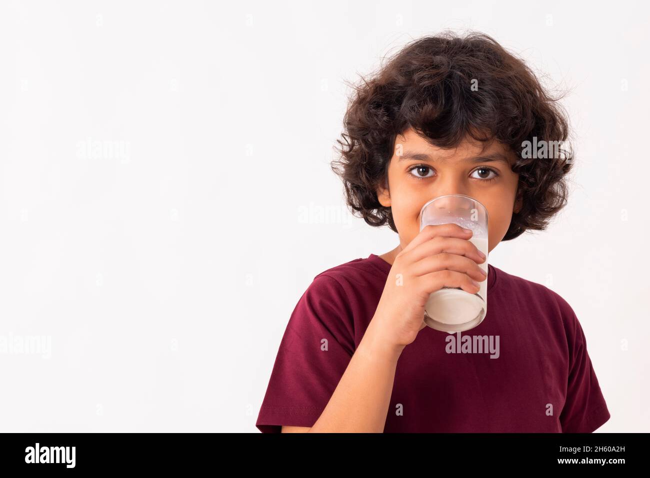 A YOUNG BOY DRINKING A GLASS OF MILK WHILE LOOKING AT CAMERA Stock Photo