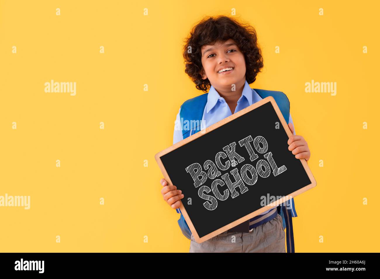 A BOY IN SCHOOL UNIFORM HAPPILY DISPLAYING MESSAGE OF BACK TO SCHOOL AFTER PANDEMIC Stock Photo