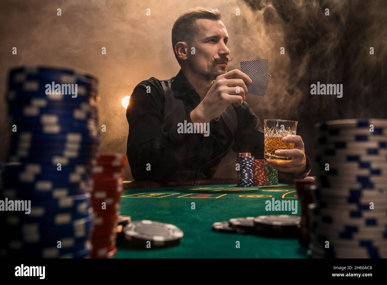 Handsome bearded man drinking whisky while playing poker Stock Photo
