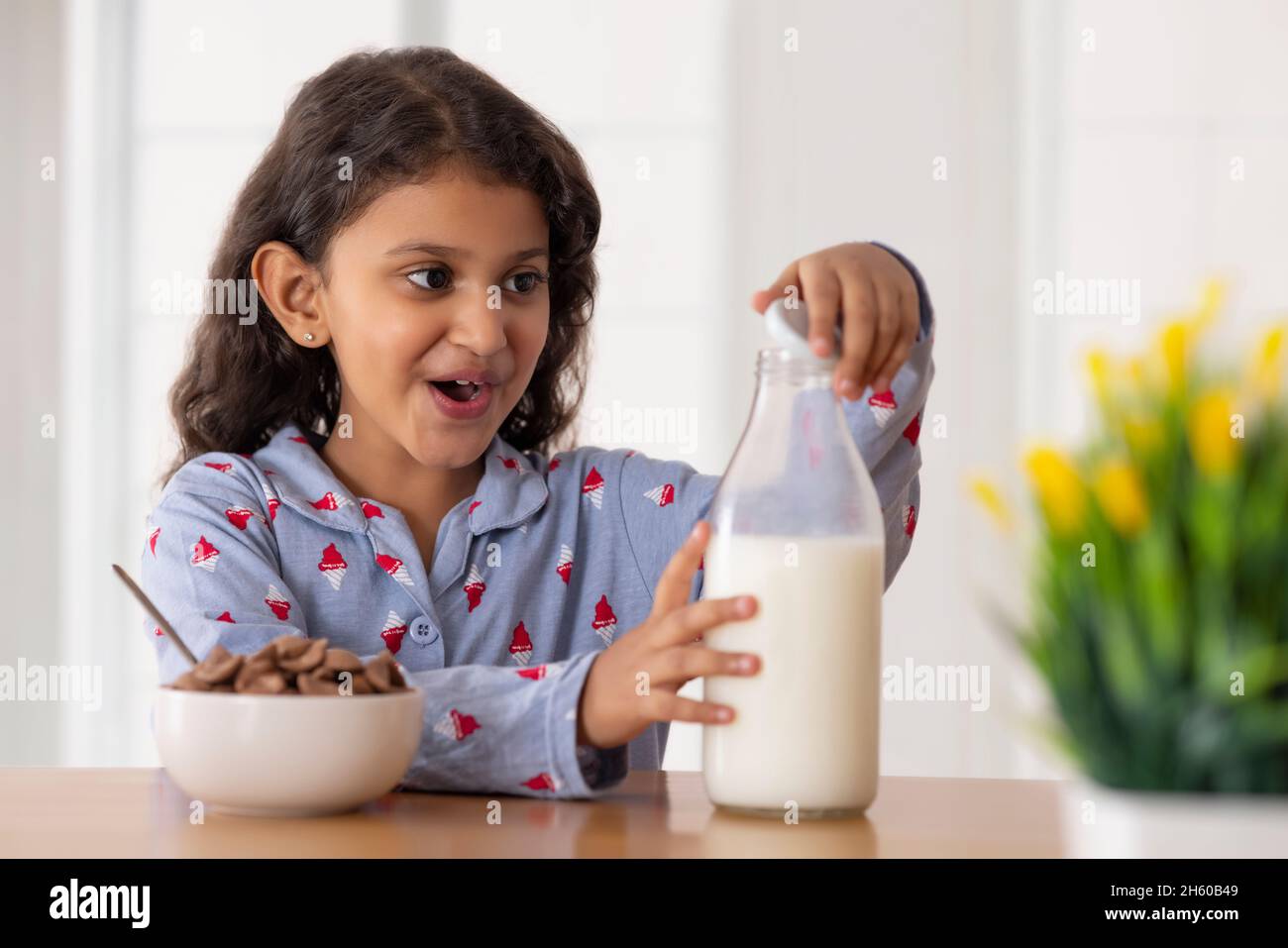 A girl opening cap of a milk bottle to pour into a bowl full of chocos