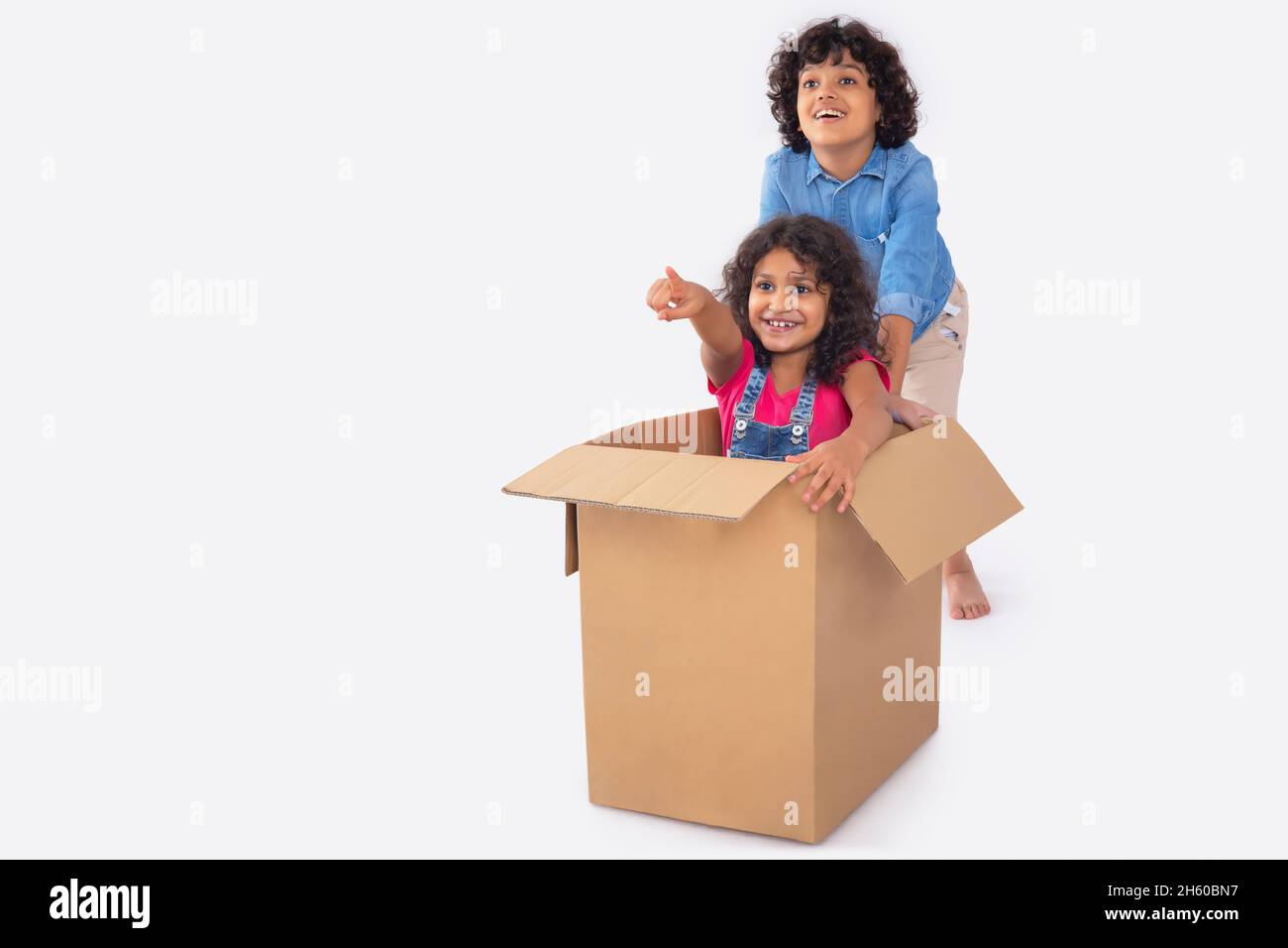 Indian beautiful girl sitting inside box and her bother moving box while playing Stock Photo