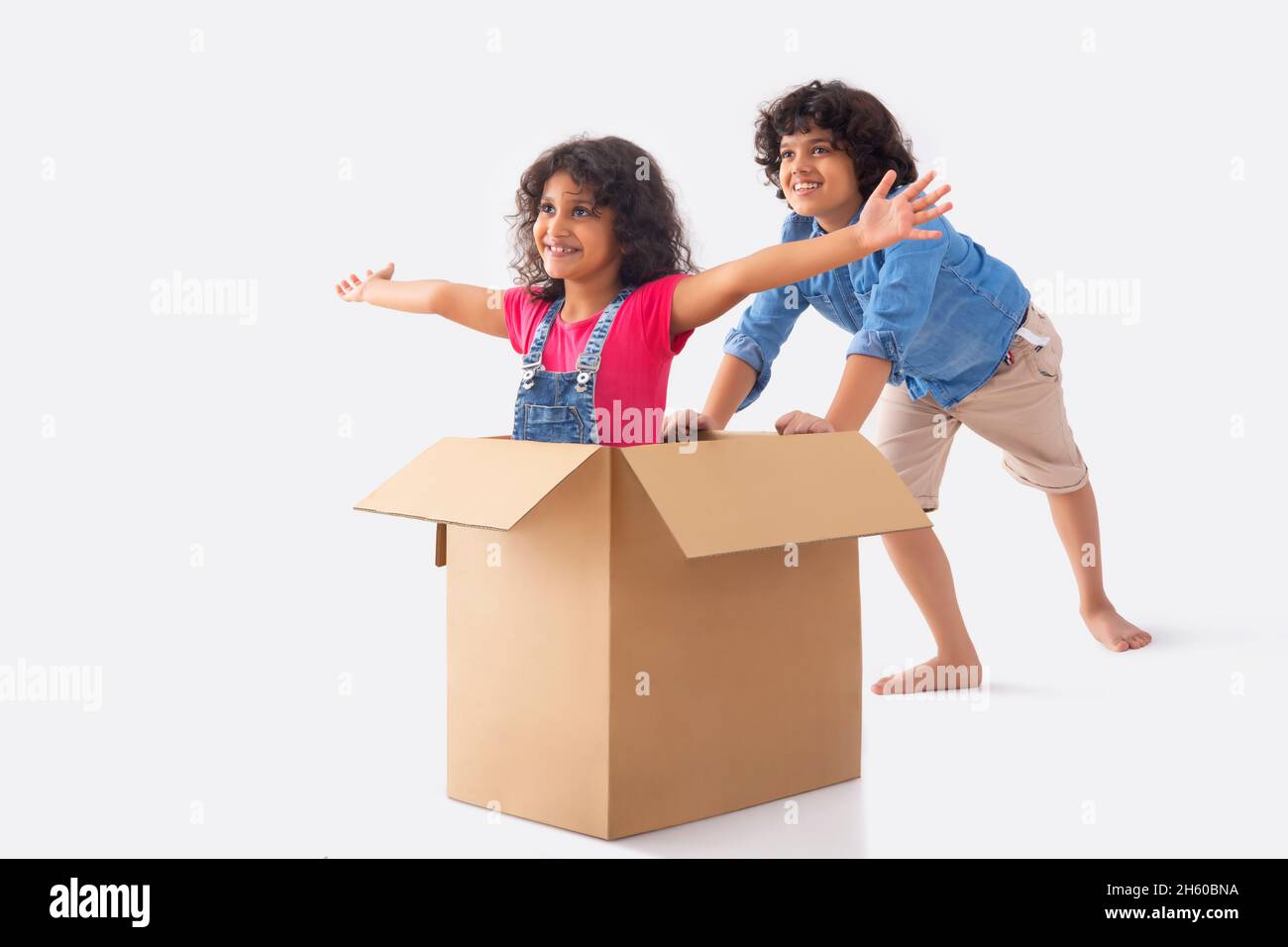 Girl sitting inside box with open arms and her bother moving box while playing Stock Photo