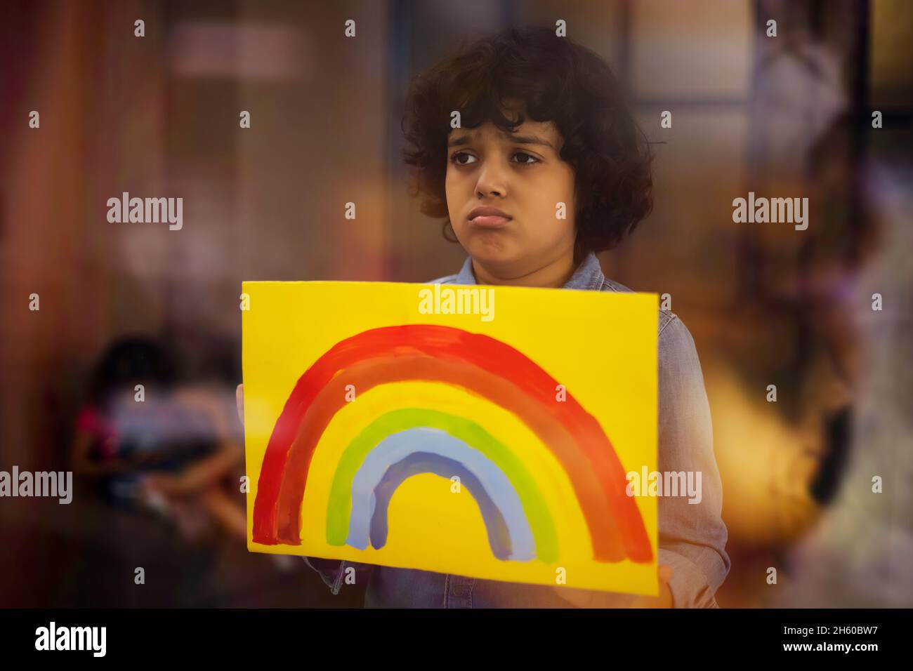 An Indian boy in sad mood showing a rainbow painting in front of camera Stock Photo