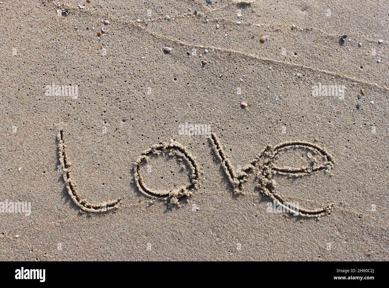 On the beach, the word Love is carved in letters in the smooth sand, which is washed away by a wave Stock Photo