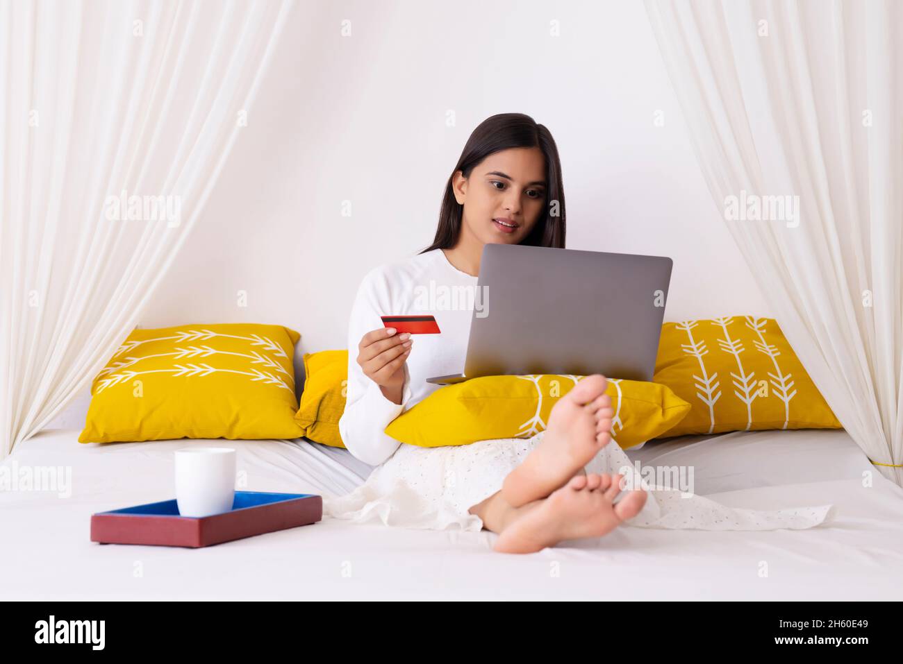 Smart Indian girl shopping online through laptop using debit card in bedroom Stock Photo