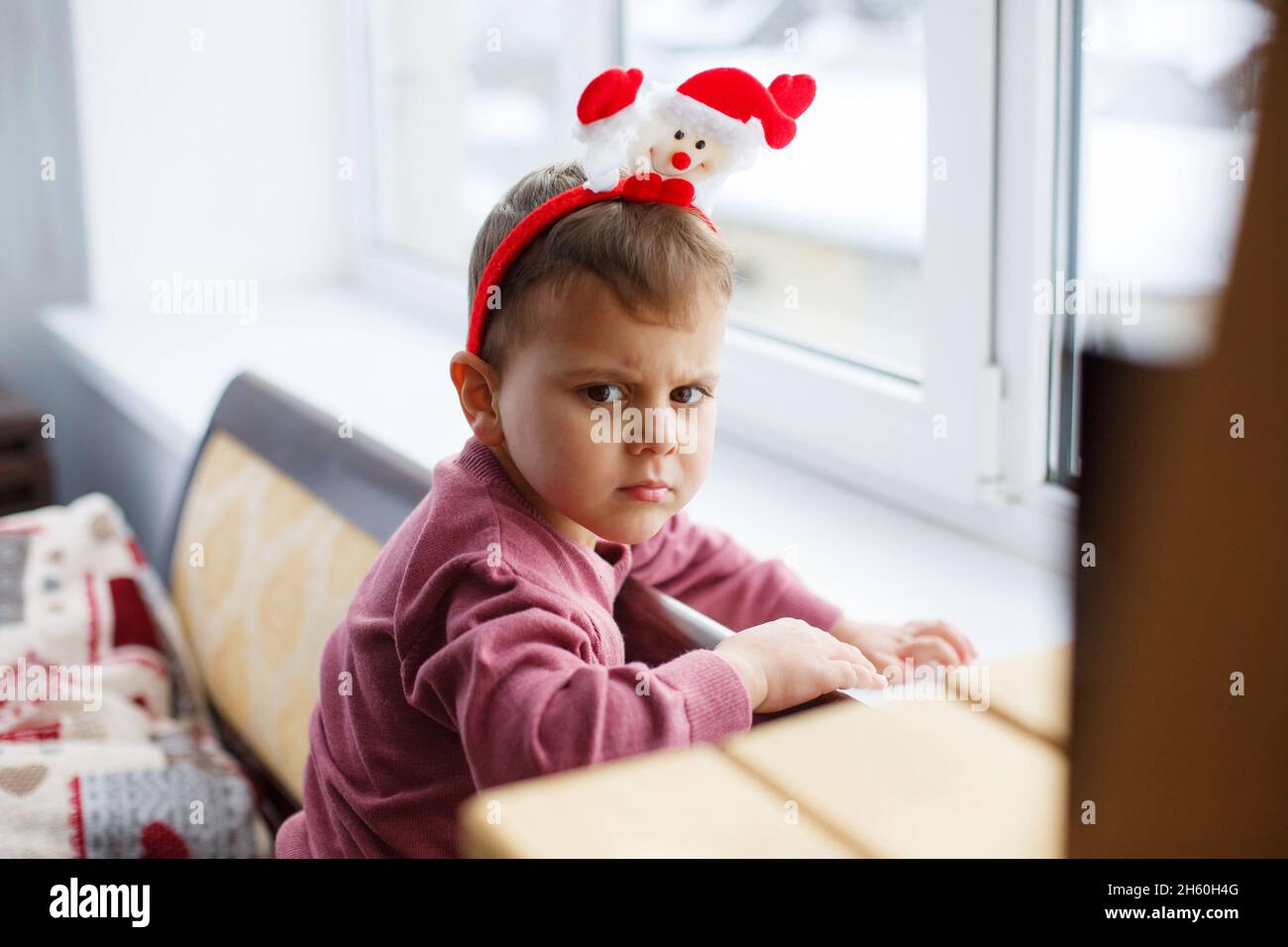 Cute angry little boy with fanny hat looking to camera. Cute toddler child near window. Stock Photo