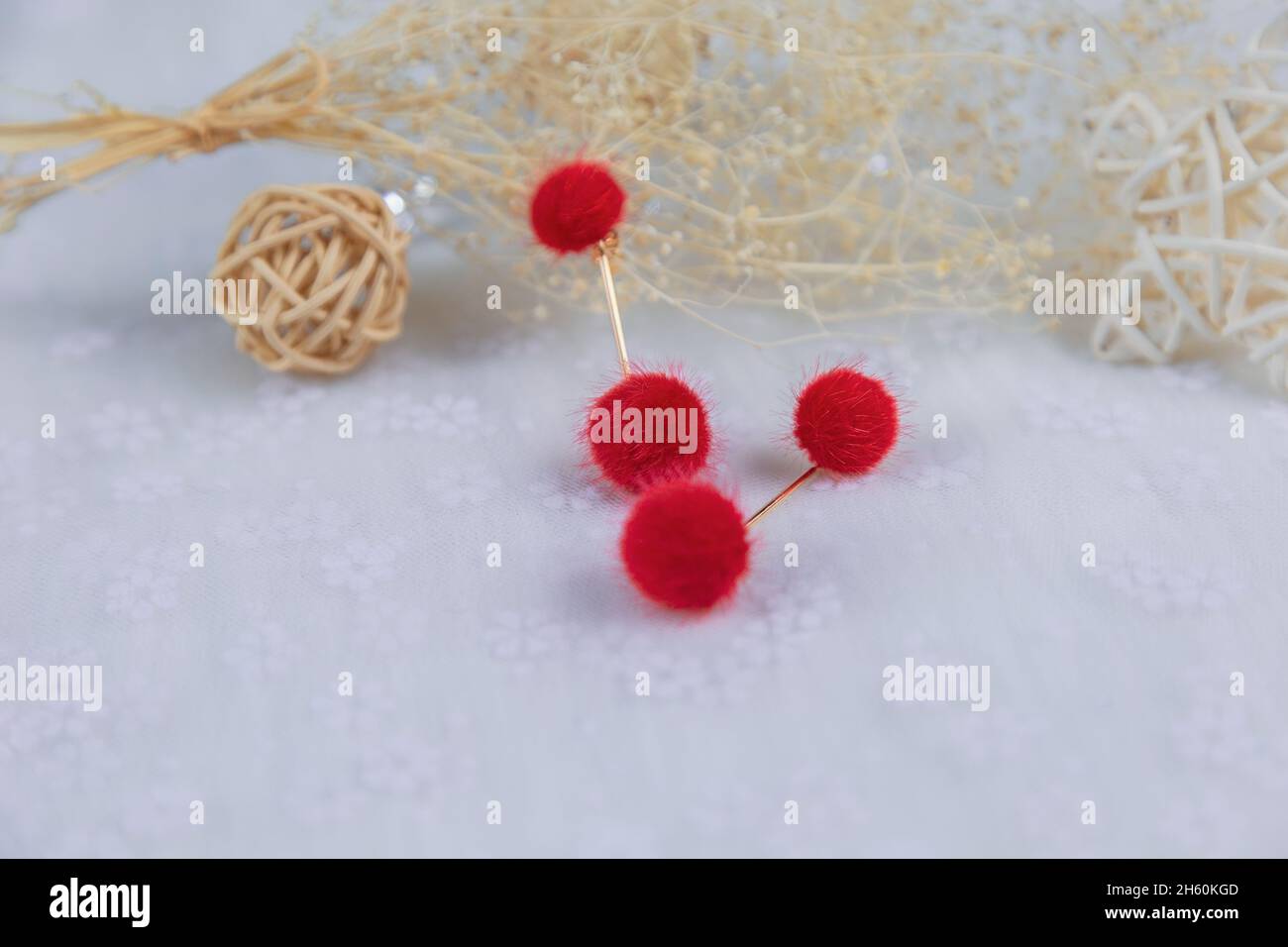 Red pompon earrings in the shape of two fluffy balls.Earrings are next to rattan products, flower specimens and other ornaments Stock Photo