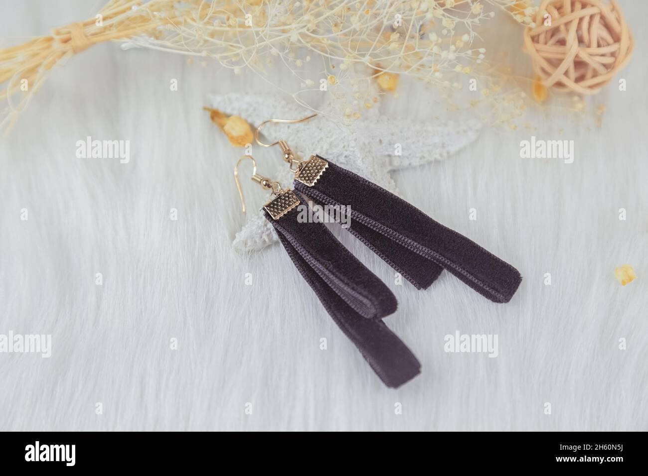 Black streamer earrings. Beside the earrings are rattan products, withered yellow bouquet specimens and other decorative objects. Stock Photo