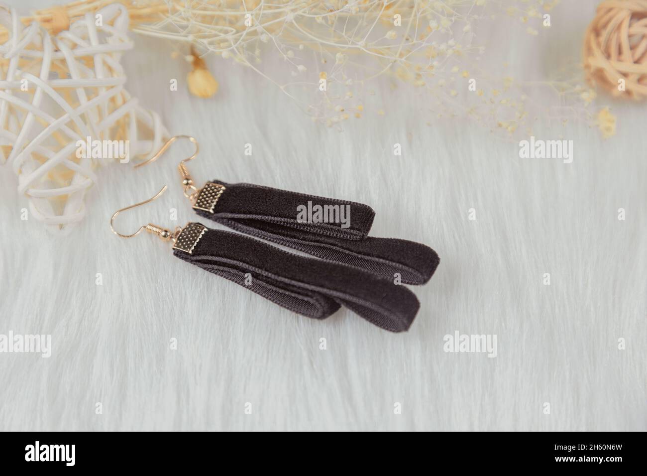 Black streamer earrings. Beside the earrings are rattan products, withered yellow bouquet specimens and other decorative objects. Stock Photo