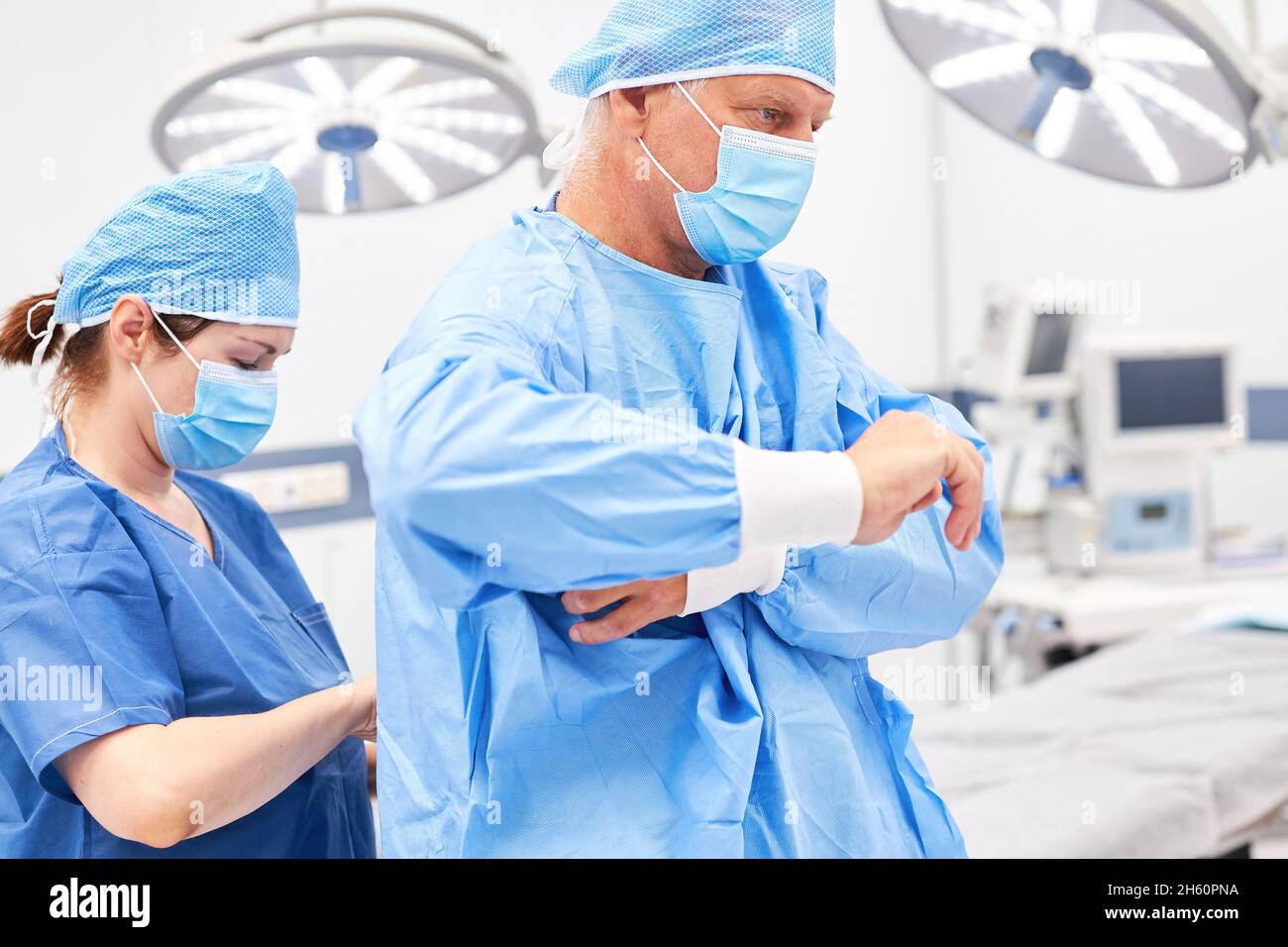 Resident doctor helps surgeon put on gown before surgery Stock Photo