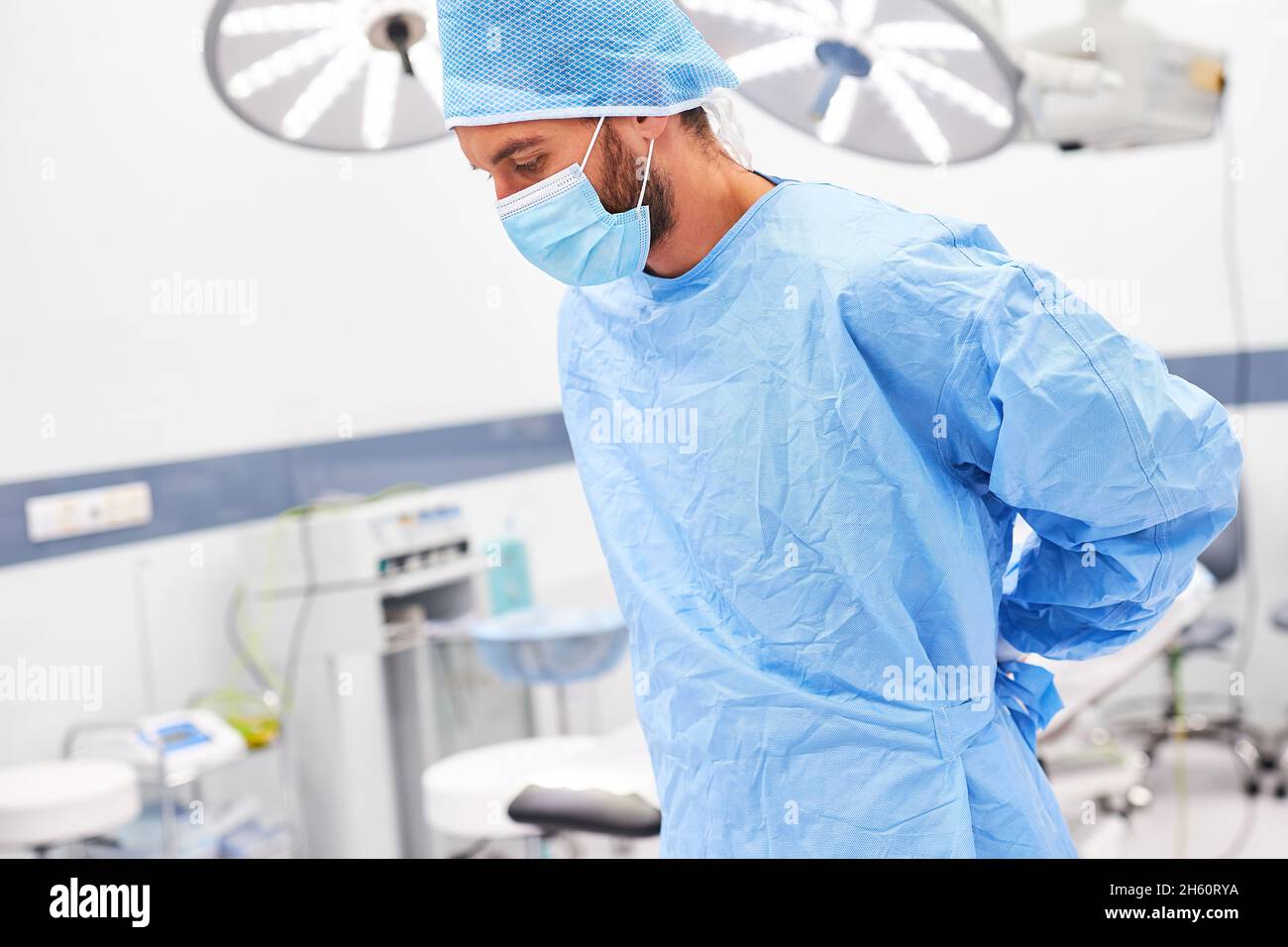 Surgeon wearing a face mask while putting on a gown as preparation for the operation in the operating room Stock Photo