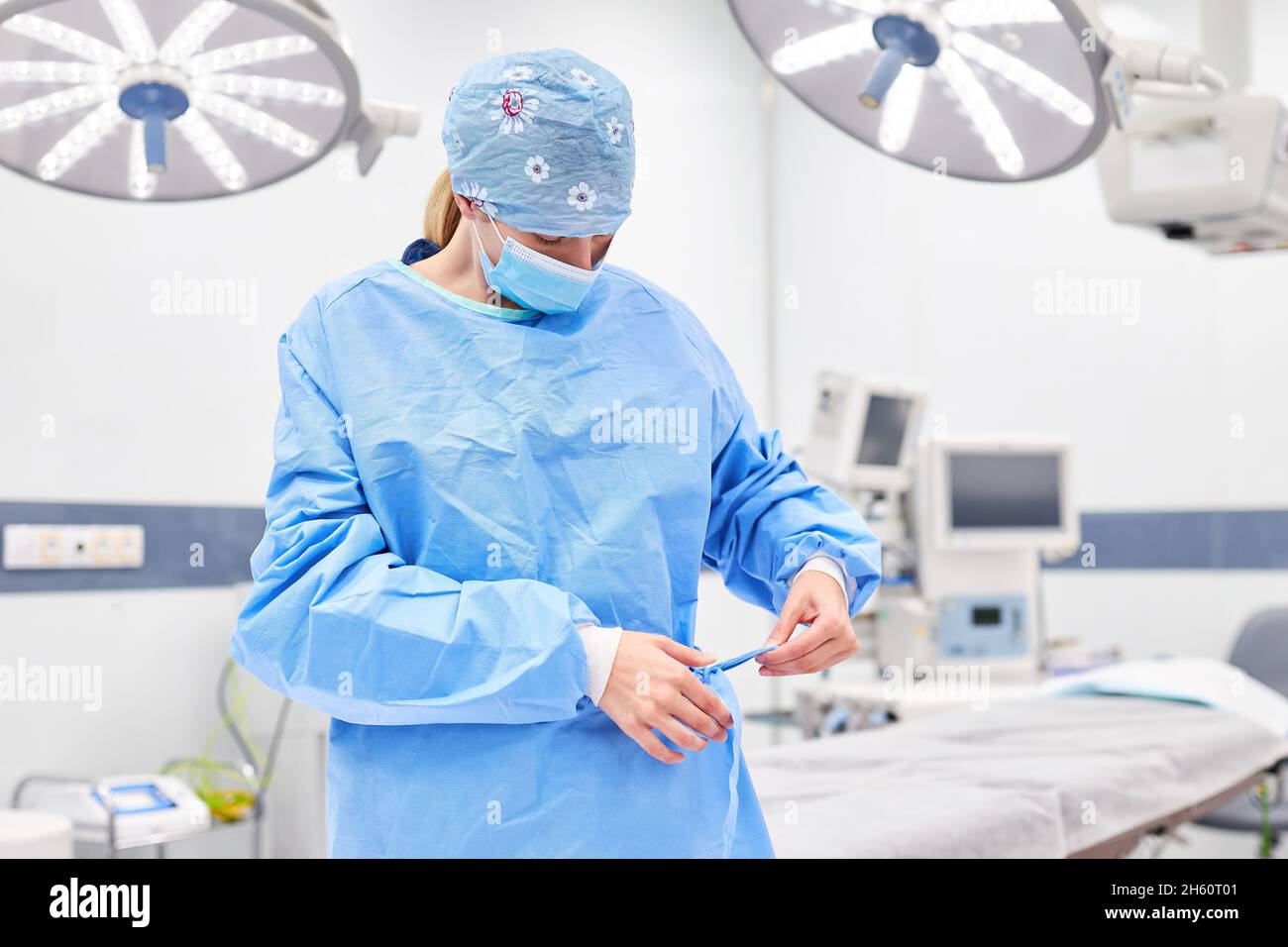 Doctor as surgeon with face mask puts on the gown before the operation in the surgery Stock Photo