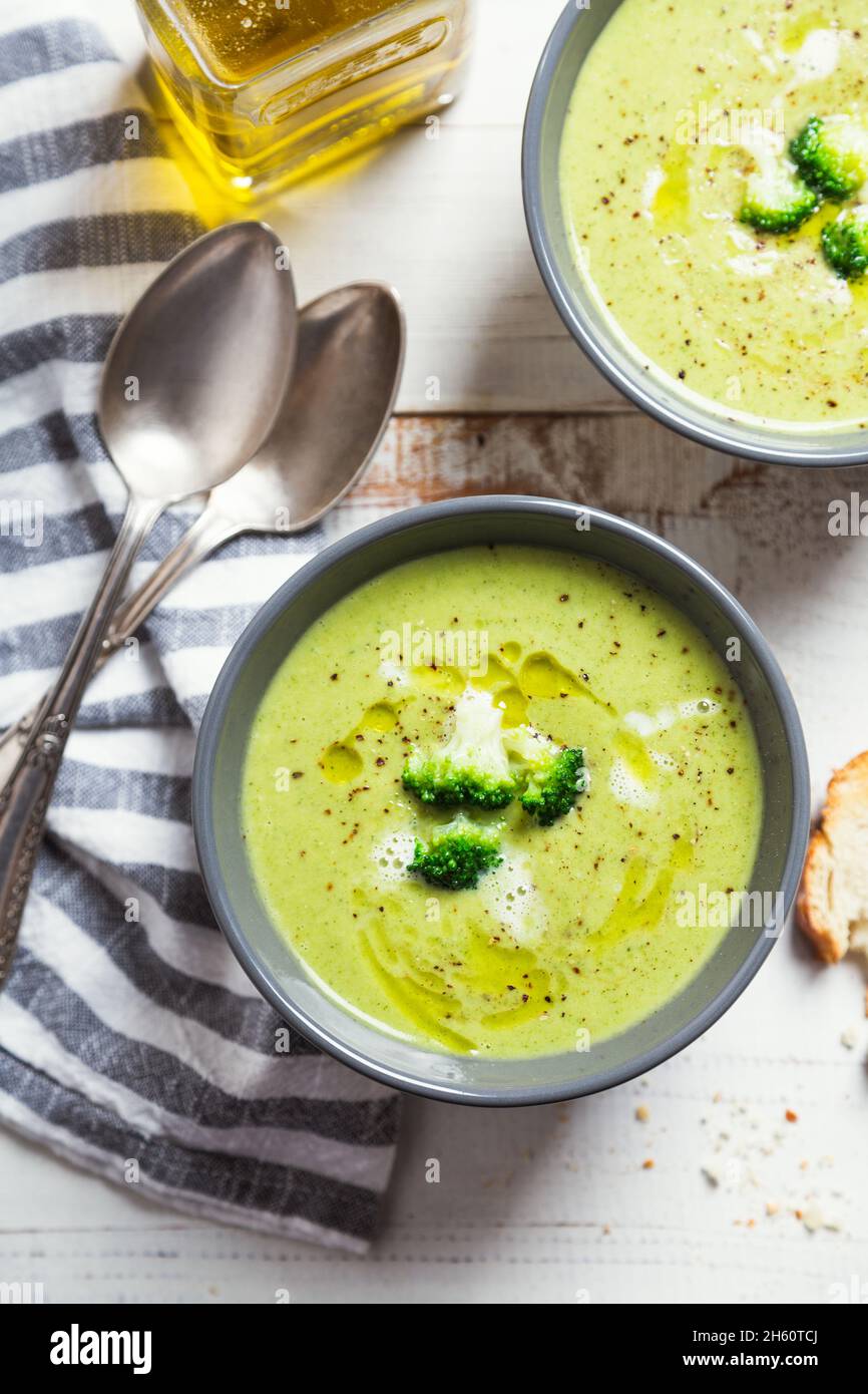 Bowls of broccoli cream soup with olive oil, pepper and toasted bread slices on a rustic white wooden table Stock Photo