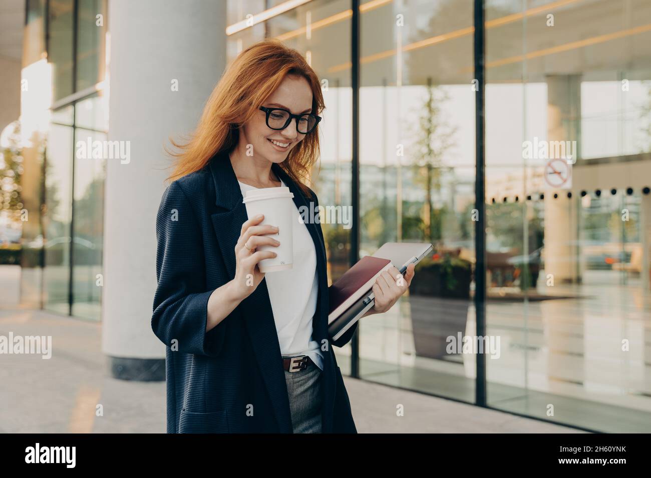 Smiling redhead woman corporate worker dressed in formal clothes drinks coffee Stock Photo