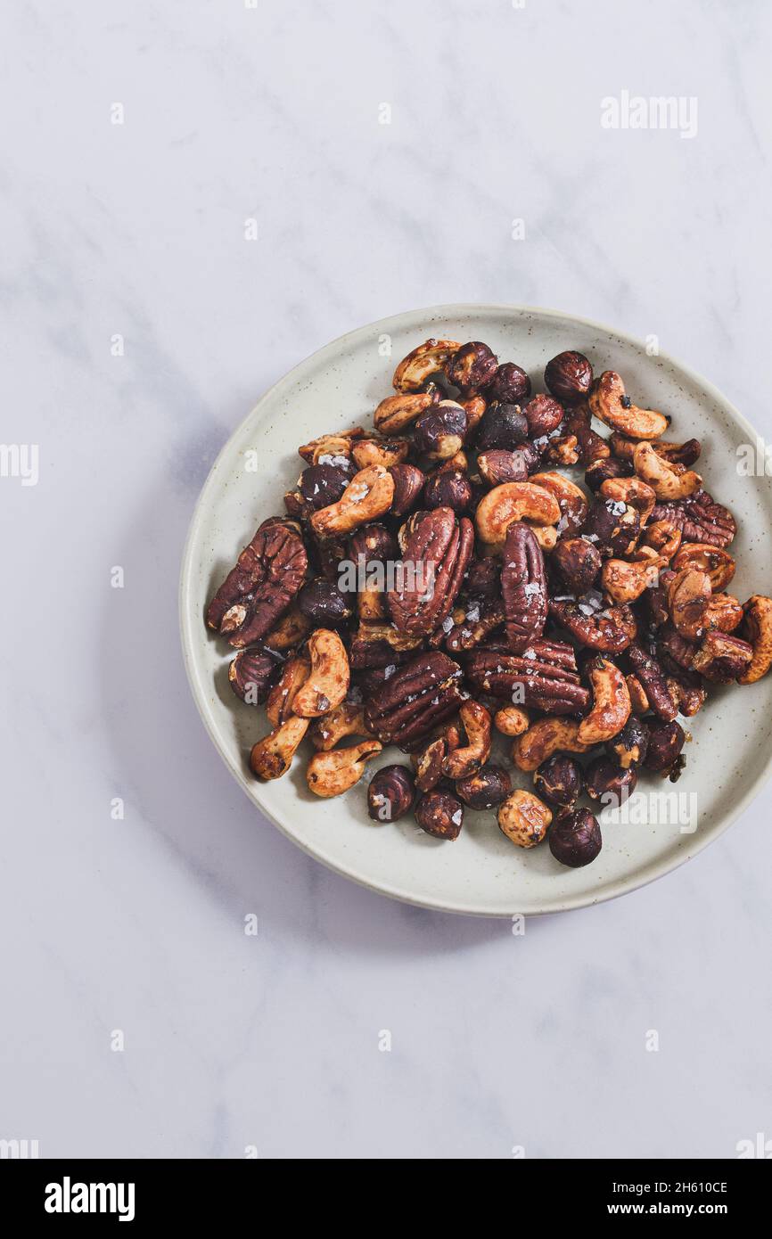 Small plate filled with a snack of roasted honey and rosemary mixed nuts (hazelnut, pecan, cashew). Stock Photo