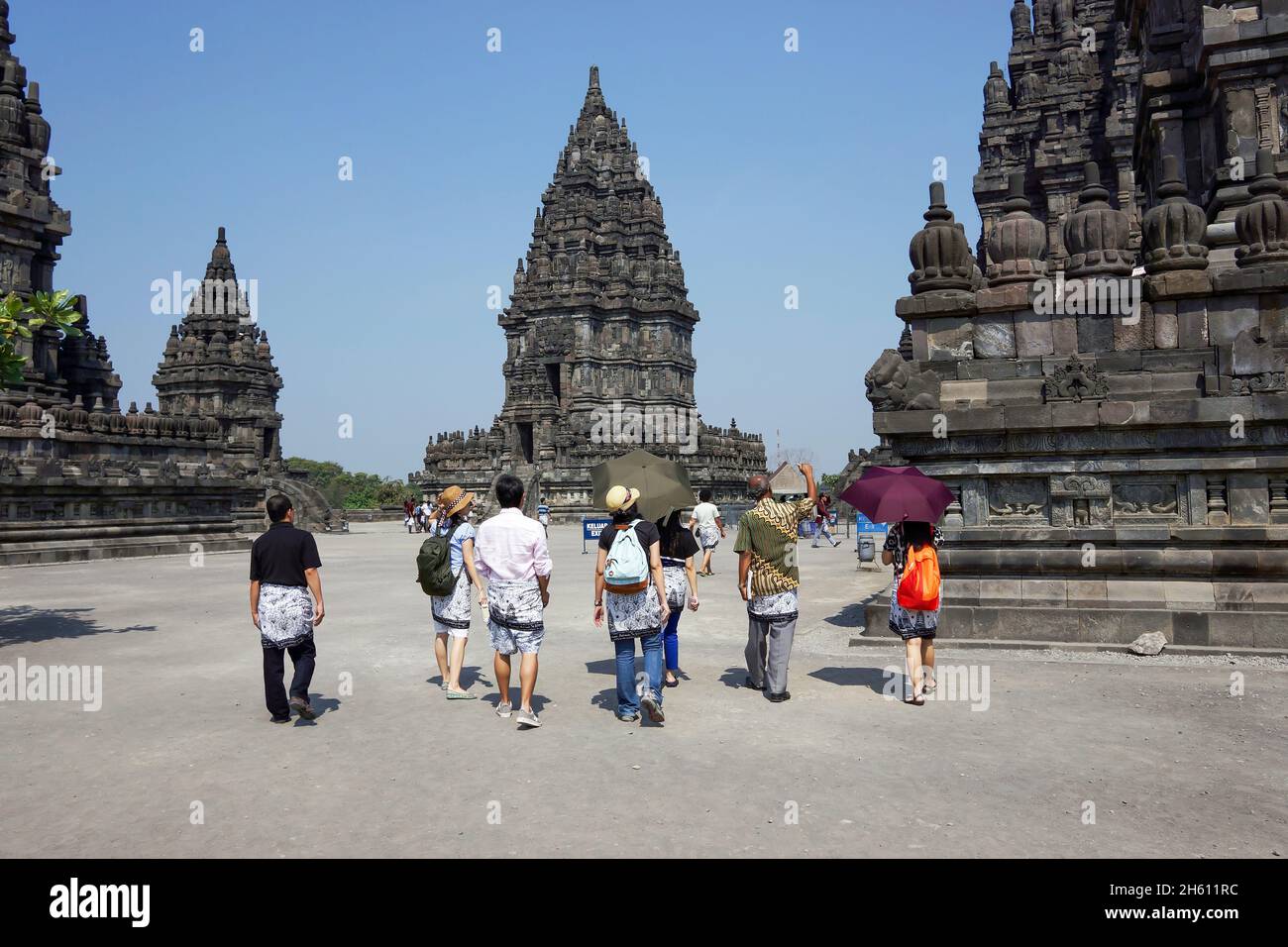 Group of Asian people with tour guide walking around ancient hindu Prambanan Temple complex. Sunny clear blue sky background. Stock Photo